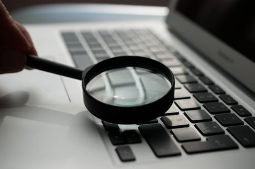 A magnifying glass on top of a laptop keyboard symbolising the identification of key customer details
