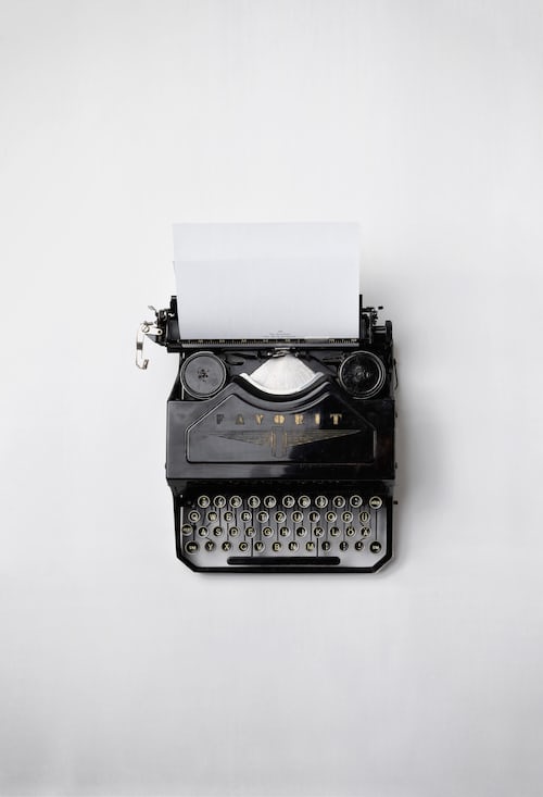A black typewriter with a piece of paper inserted in the top against a white background