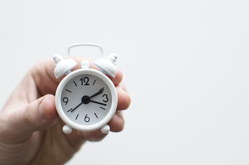 A person holding a small white alarm clock to highlight the importance of time management