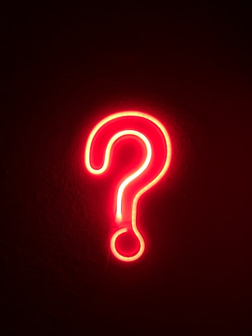 A red fluorescent question mark icon on a dark wall