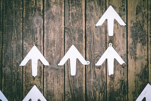 A number of upward pointing white arrows on a wooden board