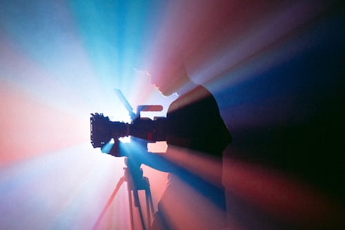A man with a video camera filming inn a dark room with lights spraying in all directions