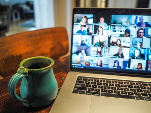 A virtual sales meeting with a number of customers on a laptop with a coffee cup on the table