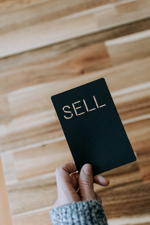 A person holding a black card saying sell on it