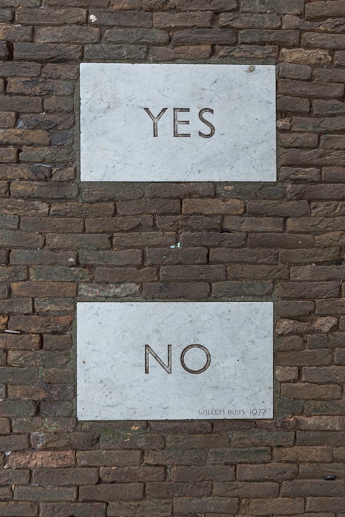 Two Yes and No placards placed on a brick wall