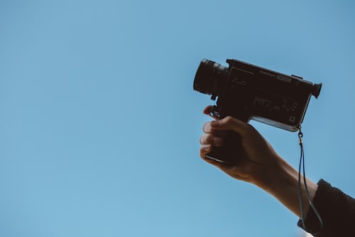 A person holding a small video camera against a blue background