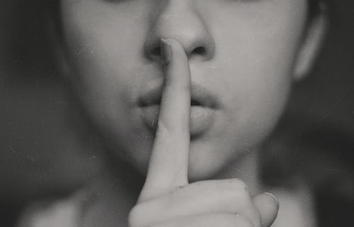 A woman with her fingers to her lips to symbolise being quiet